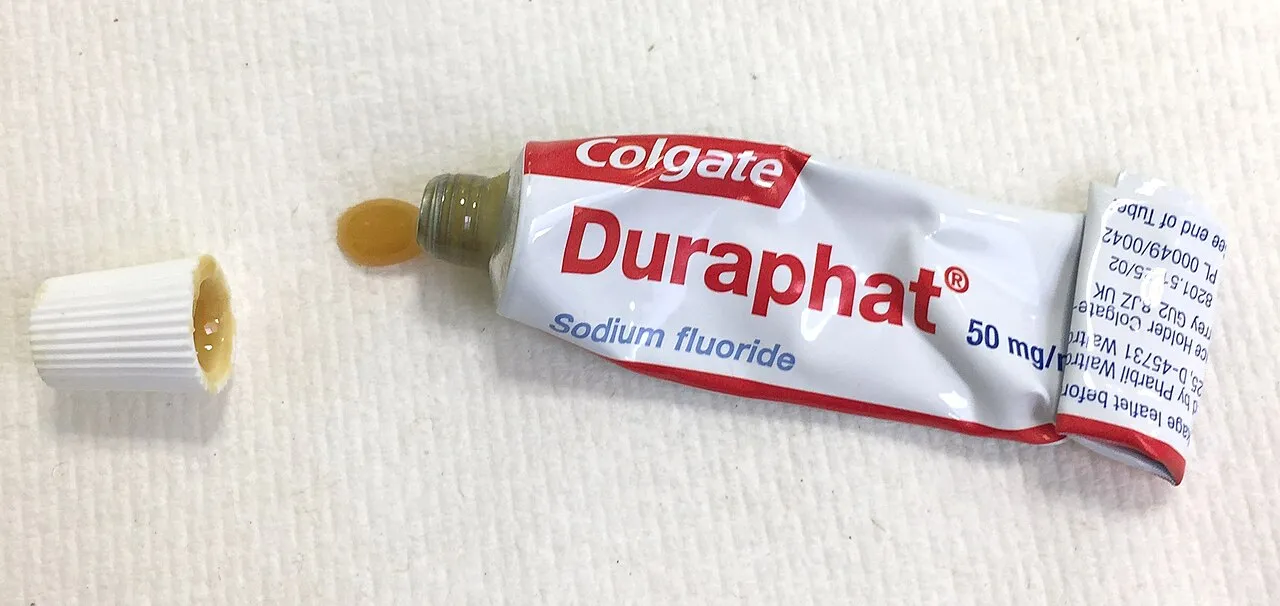 An opened tube of sodium fluoride varnish with a drop of the yellow varnish at the nozzle; varnish is one of the agents used to block exposed dentin tubules